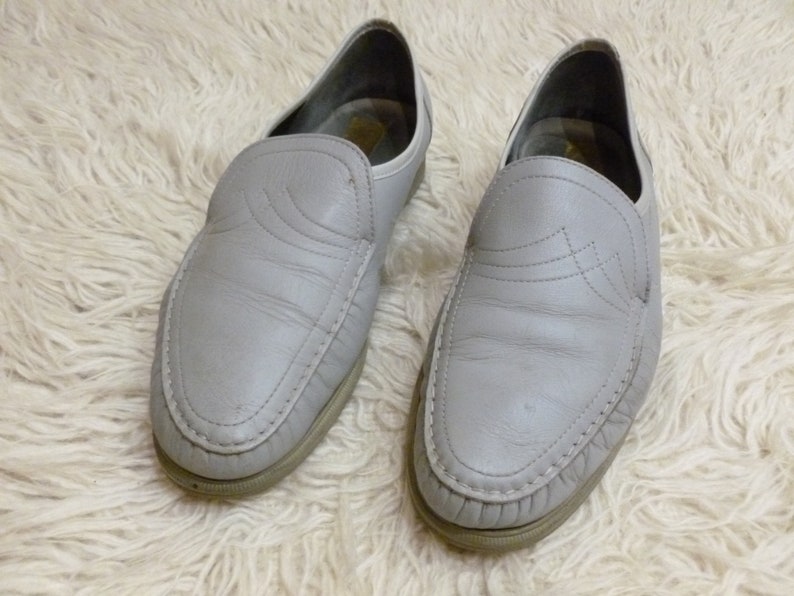May include: A pair of gray leather slip-on shoes with a decorative stitching detail on the toe.
