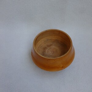 May include: A small, wooden bowl with a natural, light brown finish. The bowl has a rounded shape and a smooth, polished surface.