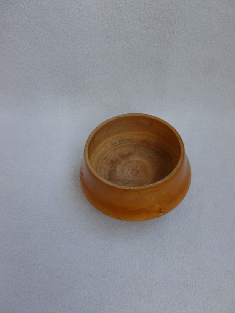 May include: A small, wooden bowl with a natural, light brown finish. The bowl has a rounded shape and a smooth, polished surface.