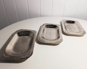 May include: Three silver rectangular serving trays with decorative edges. The trays are on a white surface.