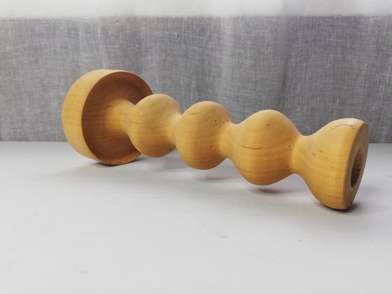 Puede incluir: Un portavelas de madera con un dise&ntilde;o &uacute;nico y retorcido. El portavelas est&aacute; hecho de madera natural y tiene un color marr&oacute;n claro.