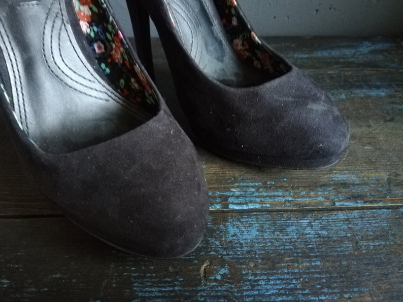 Op de afbeelding: Een paar zwarte su&egrave;de pumps met hoge hakken en een bloemenprint voering.