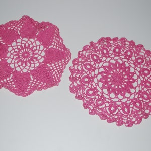 May include: Two pink crocheted doilies with intricate floral designs.