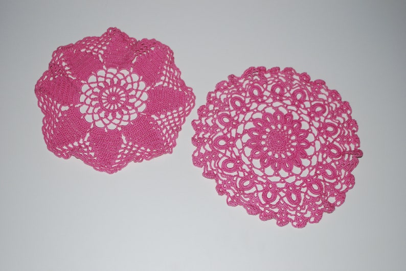 May include: Two pink crocheted doilies with intricate floral designs.