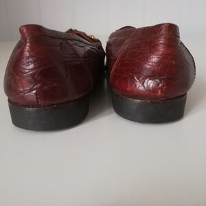 Puede incluir: Un par de mocasines de cuero marr&oacute;n con un patr&oacute;n de cocodrilo texturizado. Los mocasines tienen un detalle de hebilla dorada y una suela de goma negra.