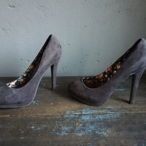 Op de afbeelding: Een paar zwarte su&egrave;de pumps met een bloemenprint voering. De hakken zijn ongeveer 10 cm hoog.