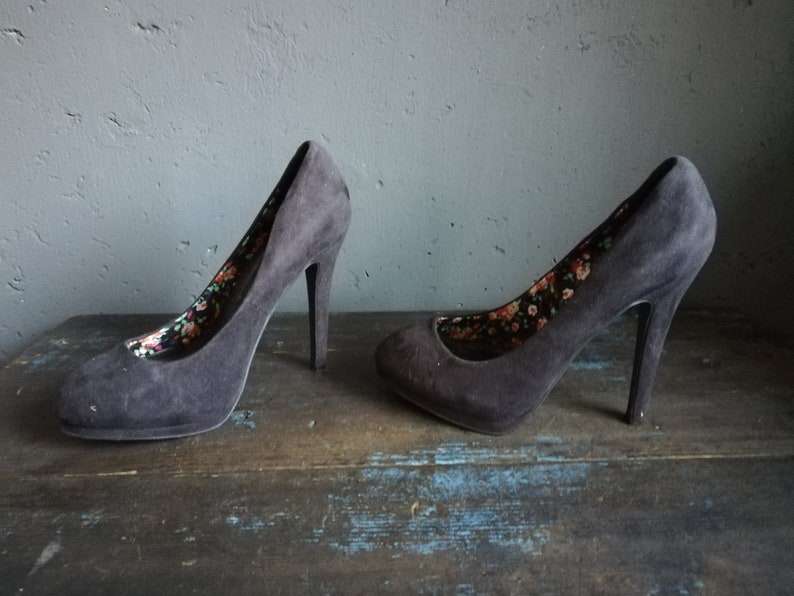 Op de afbeelding: Een paar zwarte su&egrave;de pumps met een bloemenprint voering. De hakken zijn ongeveer 10 cm hoog.