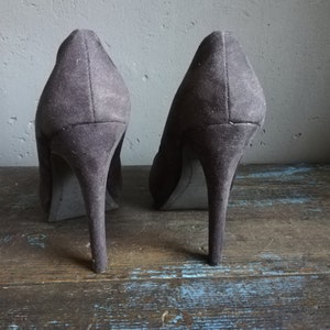 Op de afbeelding: Een paar donkergrijze su&egrave;de pumps met hoge hakken en spitse neuzen.