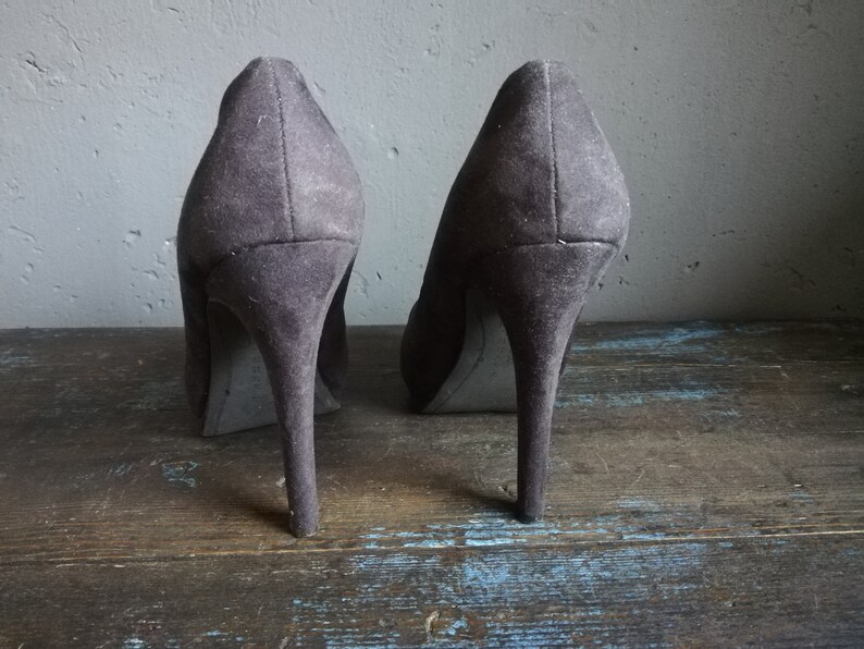 Op de afbeelding: Een paar donkergrijze su&egrave;de pumps met hoge hakken en spitse neuzen.