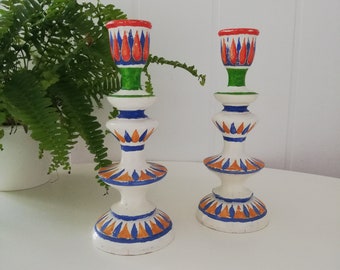 May include: A pair of white ceramic candle holders with a geometric design. The holders are decorated with orange, blue, and green accents.