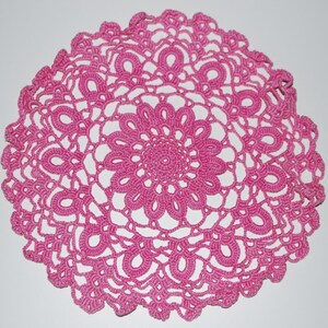 May include: A pink crocheted doily with a delicate floral design.