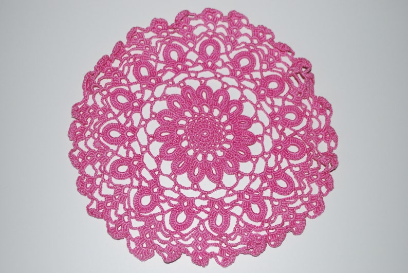 May include: A pink crocheted doily with a delicate floral design.