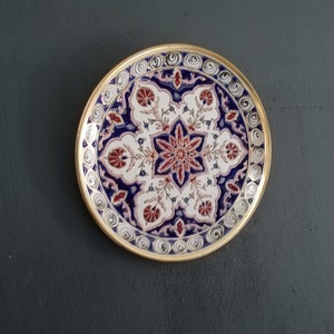 May include: A round decorative plate with a gold rim and intricate blue, white, and red floral patterns.
