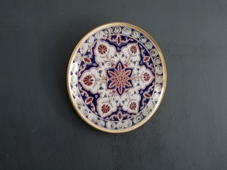 May include: A round decorative plate with a gold rim and intricate blue, white, and red floral patterns.