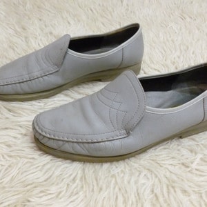 May include: A pair of gray leather slip-on shoes with a stitched detail on the toe.