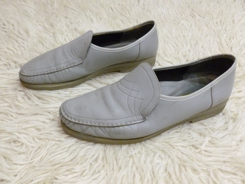 May include: A pair of gray leather slip-on shoes with a stitched detail on the toe.