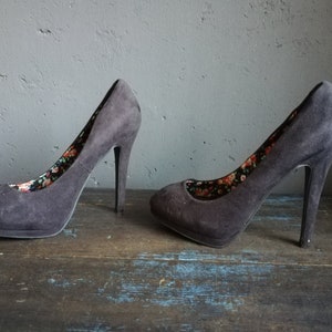 Op de afbeelding: Een paar zwarte su&egrave;de pumps met hoge hakken en een bloemenprint voering.