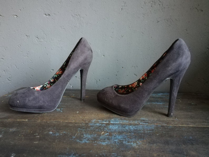 Op de afbeelding: Een paar zwarte su&egrave;de pumps met hoge hakken en een bloemenprint voering.