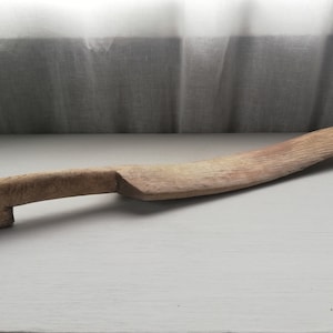 Pode incluir: Uma faca de madeira com uma lâmina curva e um cabo com um formato único. A faca é feita de madeira natural e tem um aspecto rústico.