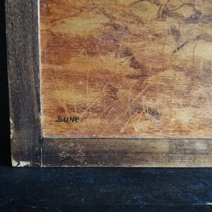May include: A close-up of a wooden framed artwork with a brown background and the word "Sune" written in black ink.