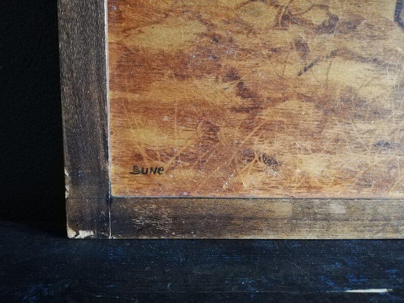 May include: A close-up of a wooden framed artwork with a brown background and the word "Sune" written in black ink.