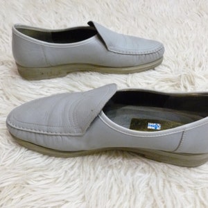 May include: A pair of gray leather slip-on shoes with a stitched seam around the toe and a small label on the inside of one shoe.