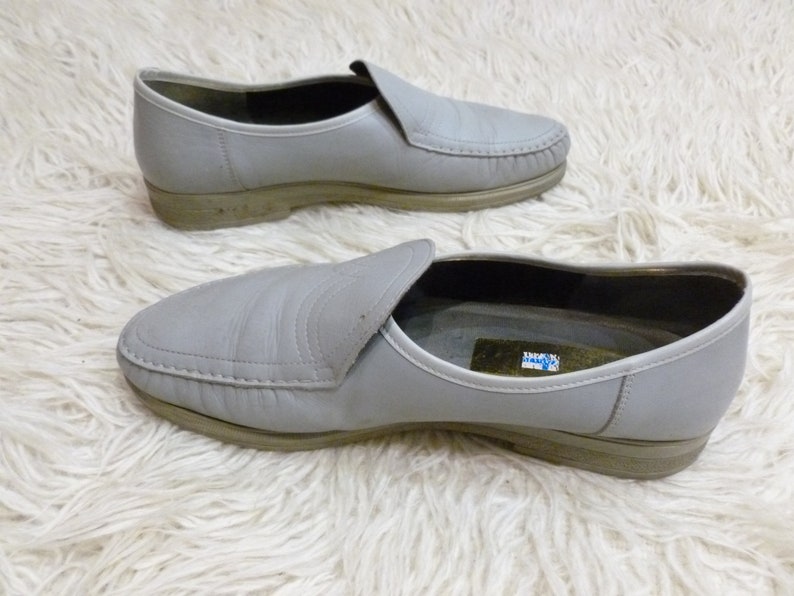 May include: A pair of gray leather slip-on shoes with a stitched seam around the toe and a small label on the inside of one shoe.