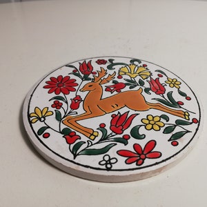 Puede incluir: Un posavasos de cer&aacute;mica blanca con un dise&ntilde;o floral colorido que presenta un ciervo en el centro. El ciervo es naranja y marr&oacute;n con detalles blancos. Las flores son rojas, amarillas y verdes.