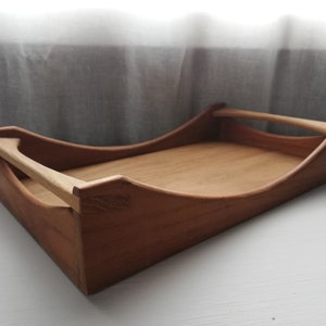 May include: A wooden serving tray with a curved design and a handle. The tray is made of light brown wood and has a natural finish.