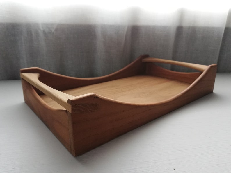 May include: A wooden serving tray with a curved design and a handle. The tray is made of light brown wood and has a natural finish.