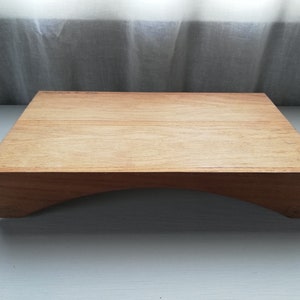 May include: A wooden serving tray with a curved base. The tray is made of light brown wood and has a smooth surface.