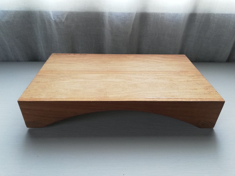 May include: A wooden serving tray with a curved base. The tray is made of light brown wood and has a smooth surface.