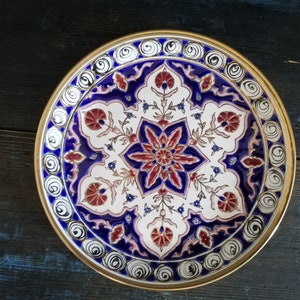 May include: A round decorative plate with a gold rim and intricate blue, white, and red floral designs.