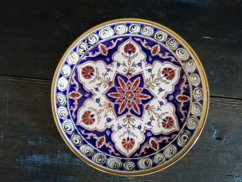 May include: A round decorative plate with a gold rim and intricate blue, white, and red floral designs.
