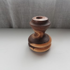 Puede incluir: Un jarrón de madera con un patrón de espiral marrón y marrón claro. El jarrón está torneado en un torno y tiene un acabado liso y pulido.