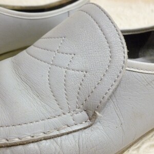 May include: A pair of gray leather slip-on shoes with a stitched design on the front. The shoes have a rounded toe and a low heel.