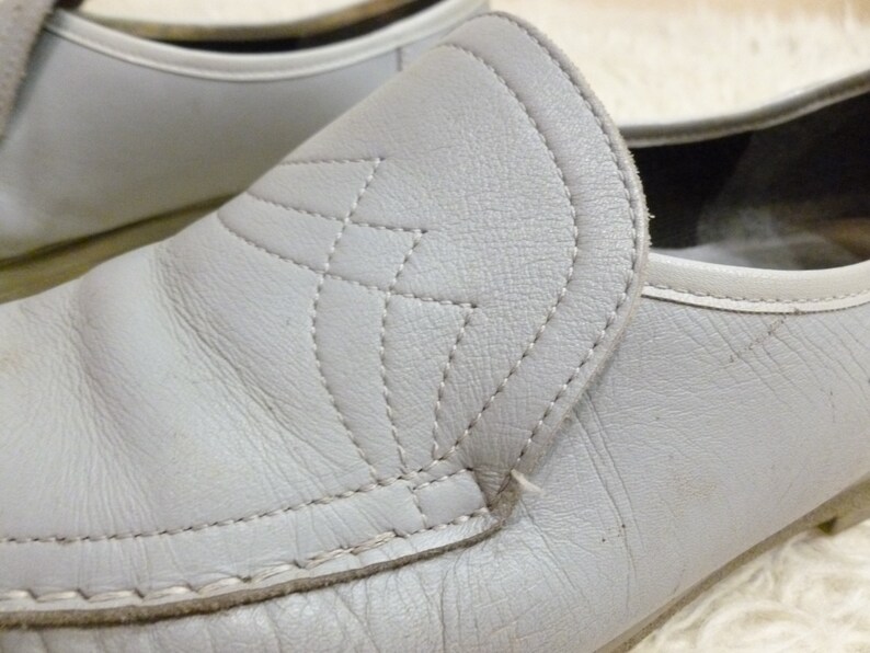 May include: A pair of gray leather slip-on shoes with a stitched design on the front. The shoes have a rounded toe and a low heel.