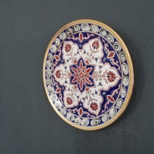 May include: A decorative ceramic plate with a blue, white, and red floral design. The plate has a gold rim and is perfect for adding a touch of elegance to any home.