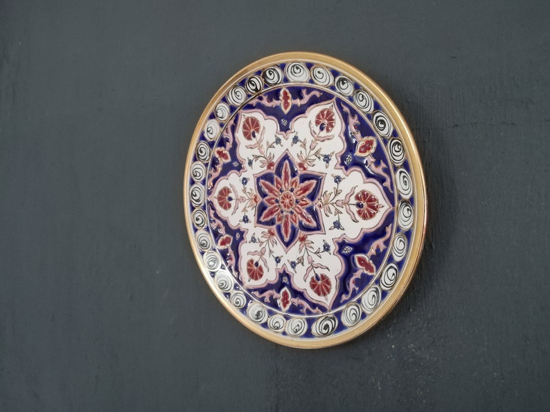 May include: A decorative ceramic plate with a blue, white, and red floral design. The plate has a gold rim and is perfect for adding a touch of elegance to any home.