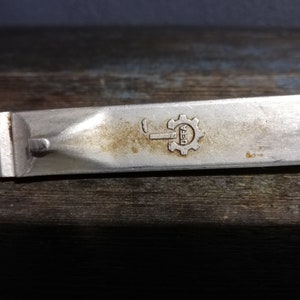 Puede incluir: Primer plano de una herramienta de metal plateado con un engranaje y la palabra "DEFA" estampada.