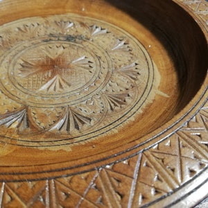 May include: A round wooden serving tray with intricate carved designs. The tray has a center circle with a starburst pattern and a border of repeating geometric shapes.