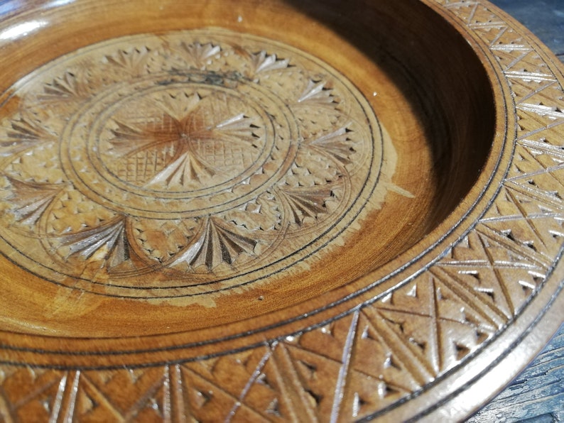 May include: A round wooden serving tray with intricate carved designs. The tray has a center circle with a starburst pattern and a border of repeating geometric shapes.