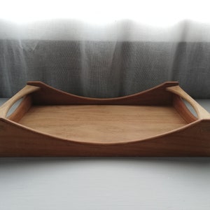 May include: A wooden serving tray with two curved handles. The tray is made of light brown wood and has a natural finish.