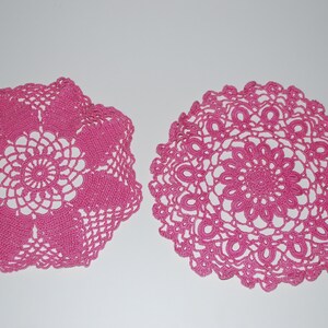 May include: Two pink crocheted doilies, one with a circular design and the other with a square design.