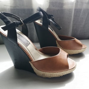 May include: A pair of brown and black wedge sandals with a peep toe and a jute platform. The sandals have a black ankle strap with a buckle closure. The brand name "Anled" is visible on the insole.