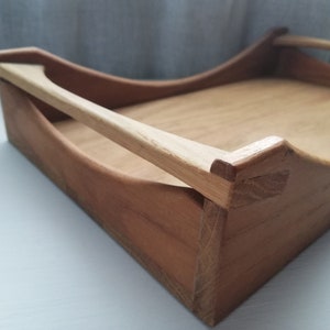 May include: A wooden tray with a natural finish and a single handle. The tray is made of light brown wood and has a slightly curved shape.