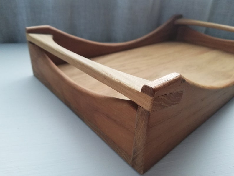 May include: A wooden tray with a natural finish and a single handle. The tray is made of light brown wood and has a slightly curved shape.