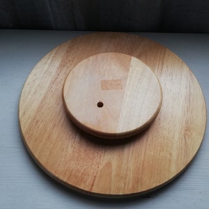 Puede incluir: Un soporte para tartas de madera de dos niveles. El nivel superior es más pequeño que el nivel inferior y tiene un agujero en el centro. Ambos niveles son de madera marrón claro.