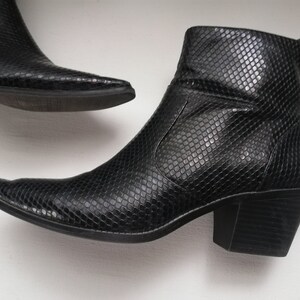 Może przedstawiać: Para czarnych kowbojskich but&oacute;w ze sk&oacute;ry wężowej z ostrym noskiem i blokowym obcasem.