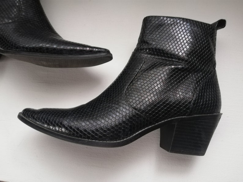 Może przedstawiać: Para czarnych kowbojskich but&oacute;w ze sk&oacute;ry wężowej z ostrym noskiem i blokowym obcasem.